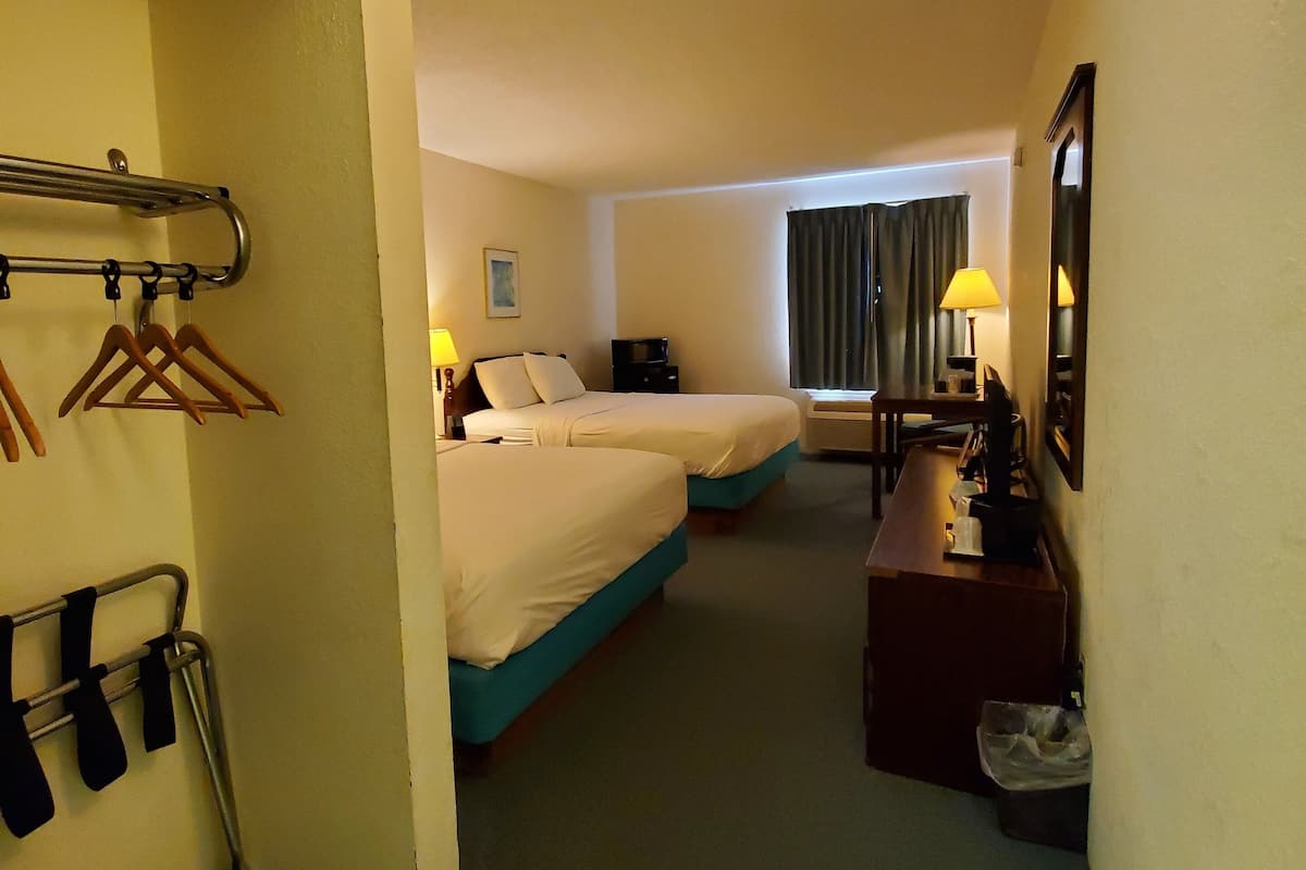 Ett hotellrum med två sängar, ett skrivbord, en stol, en lampa och ett fönster med gardiner.