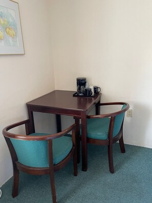 A small dining area with a dark wooden table and two teal chairs. A coffee maker and a mug are on the table. - Up North Hotel (formerly Voyager Inn) (St Ignace)