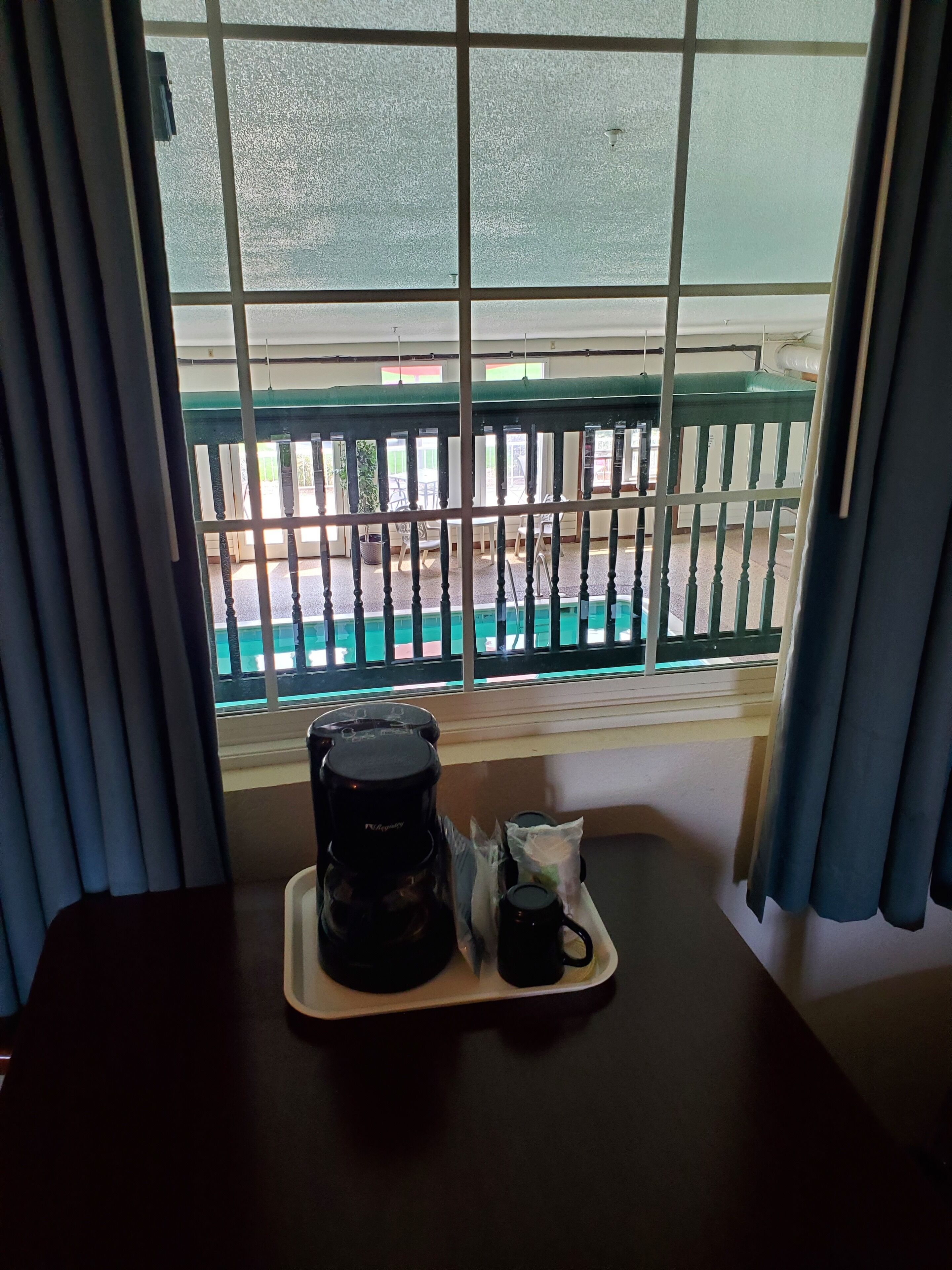 Una habitación con ventana que da a una zona de piscina, una cafetera y una taza sobre una bandeja.