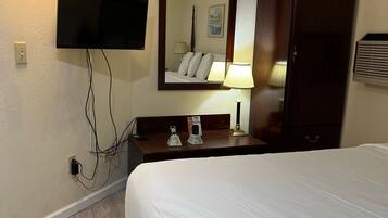 A hotel room with a bed, a TV mounted on the wall, a bedside table with a lamp, a mirror, and a wardrobe.