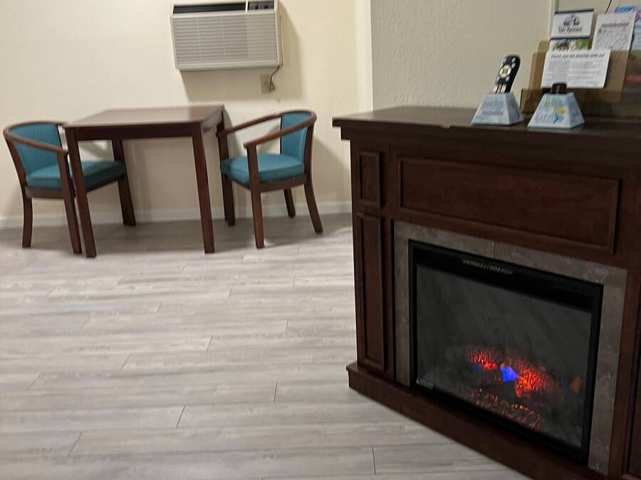 A living room with a fireplace, two wooden tables, two blue chairs, a mounted TV, and an air conditioning unit on the wall.