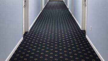A hotel hallway with a patterned carpet, light blue walls, and doors leading to rooms.