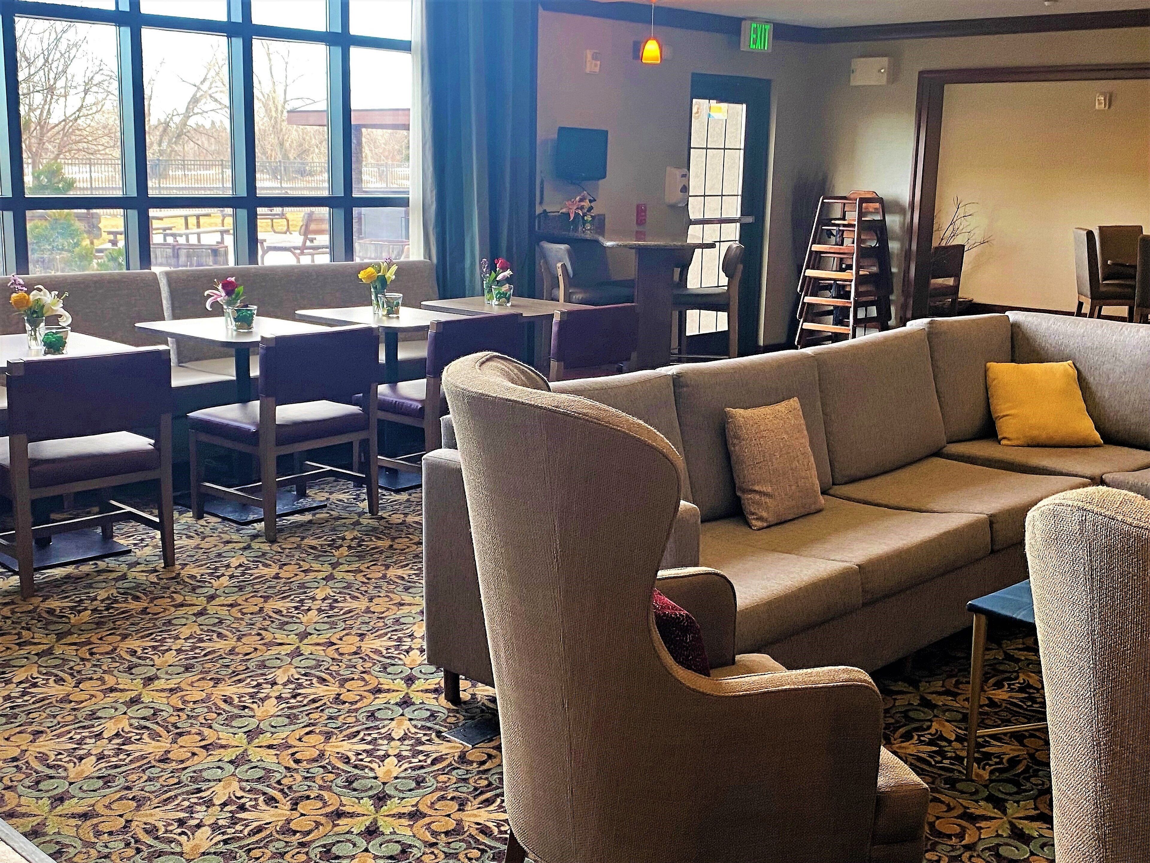 Een hotelhal met een kamerbreed tapijt, een bank, stoelen en tafels met bloemdecoraties.
