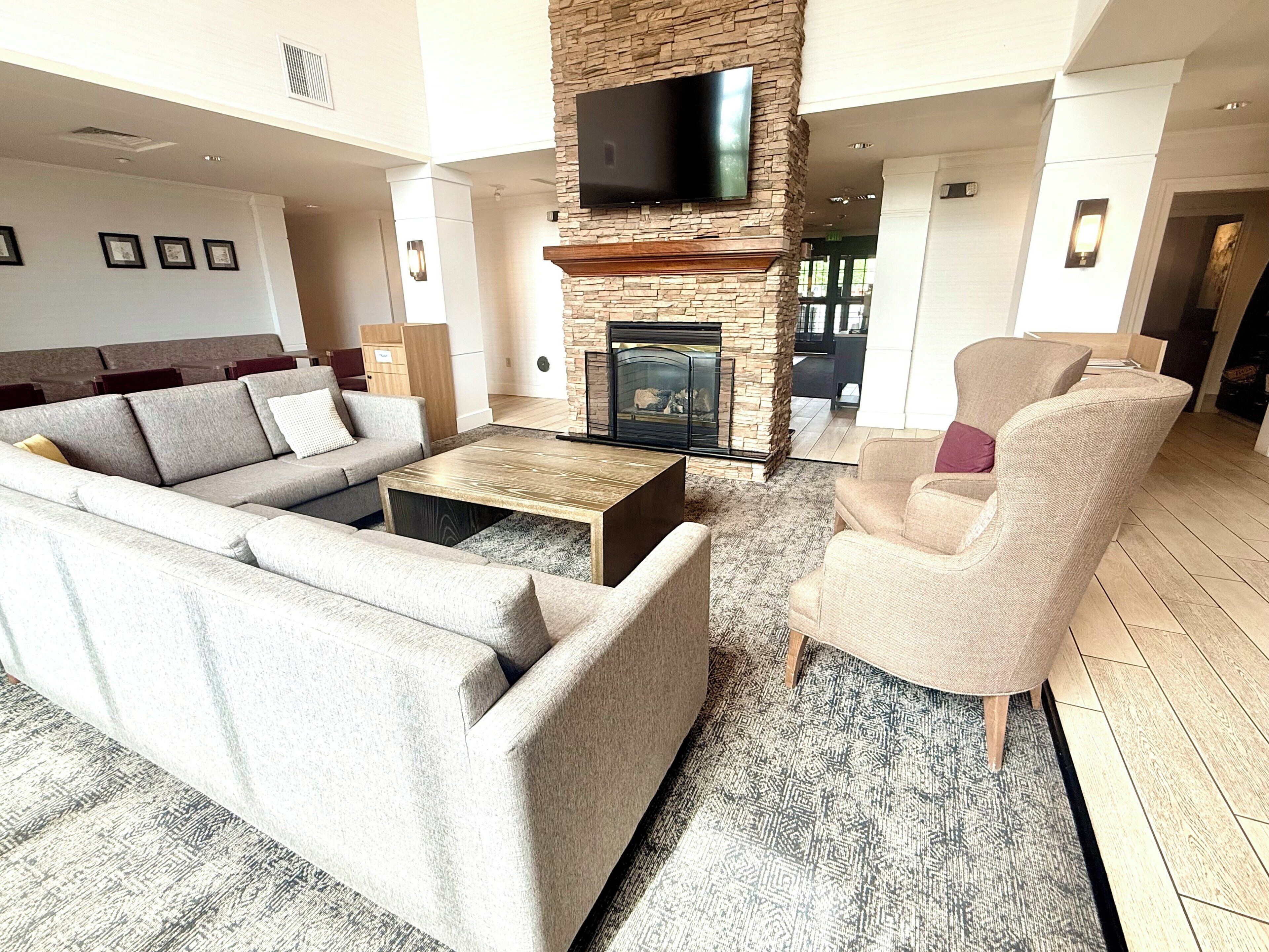 A spacious living room with a stone fireplace, a flat-screen TV mounted on the wall, and a large sectional sofa.