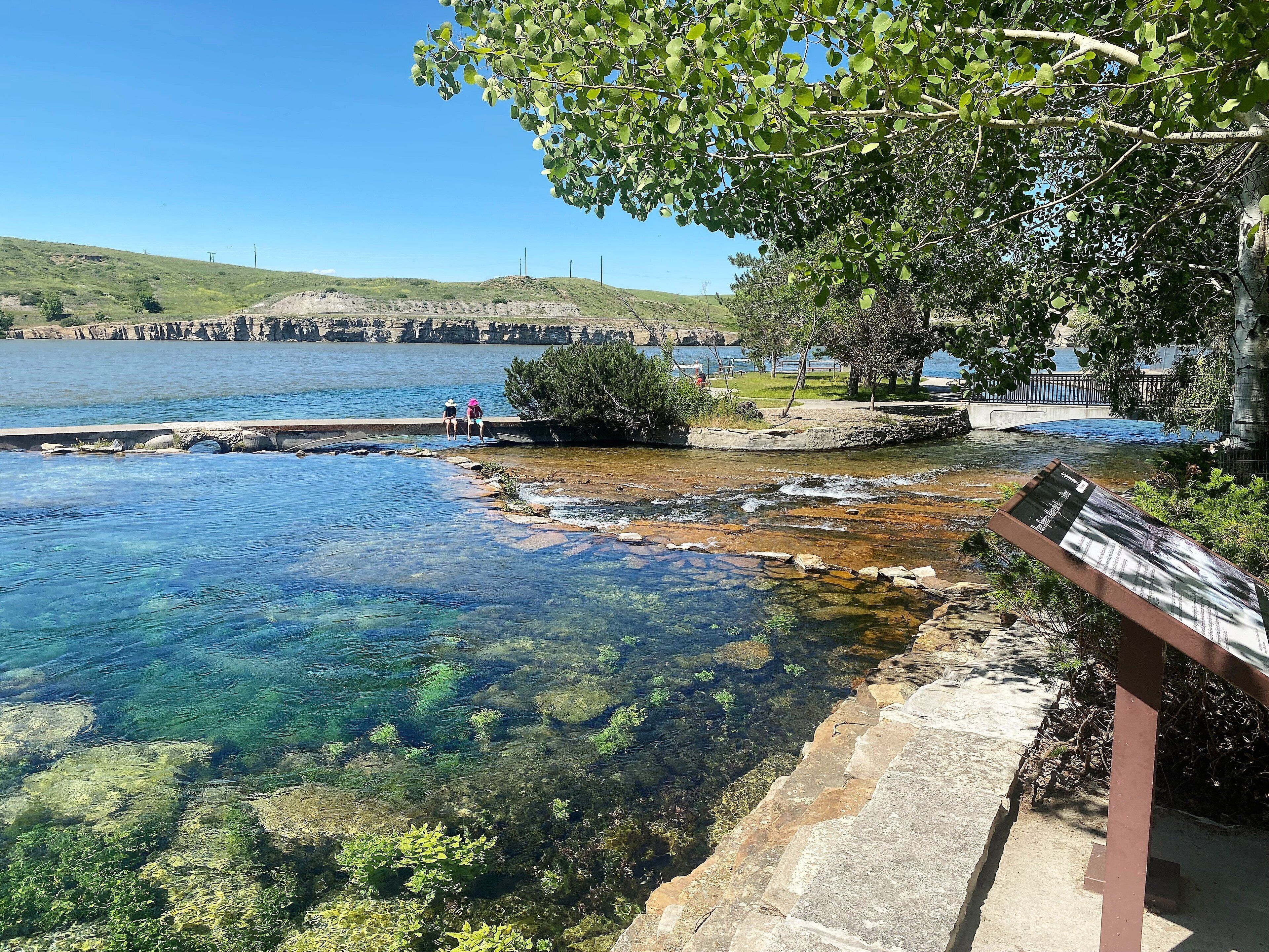 On peut clairement voir une rivière, un pont de pierre, une jetée en bois et un banc.
