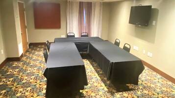A conference room with a long table covered by black cloths, patterned carpet, and a television mounted on the wall.