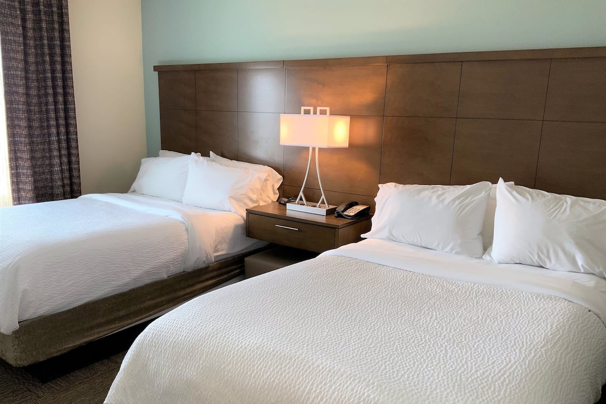 A hotel room with two beds, a nightstand with a lamp, and a telephone.