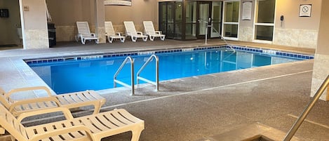 An indoor swimming pool with clear lane markings, lounge chairs, and a 'Use at your own risk' sign.