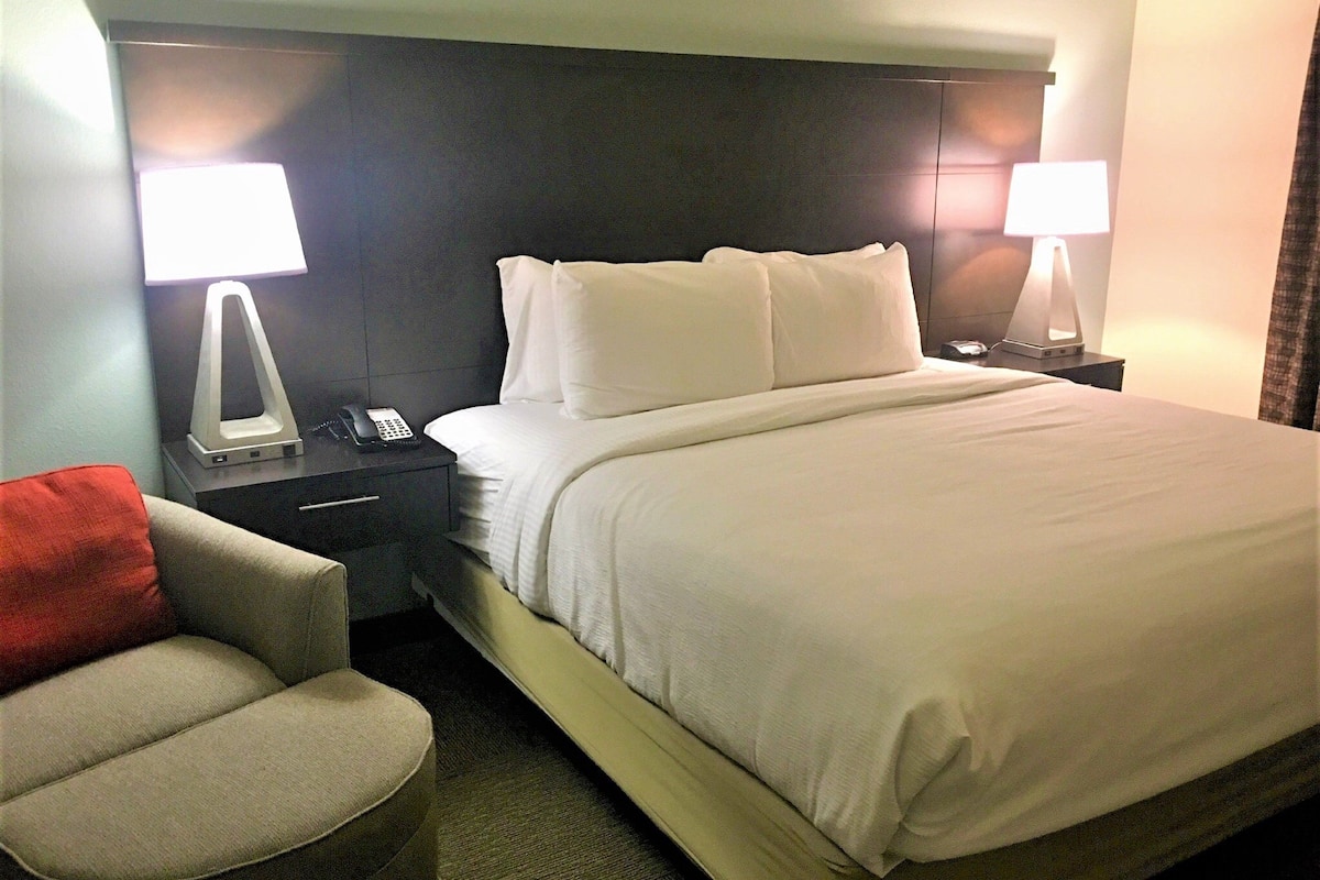 A hotel room with a bed, nightstands, a lamp, a chair, and a phone.