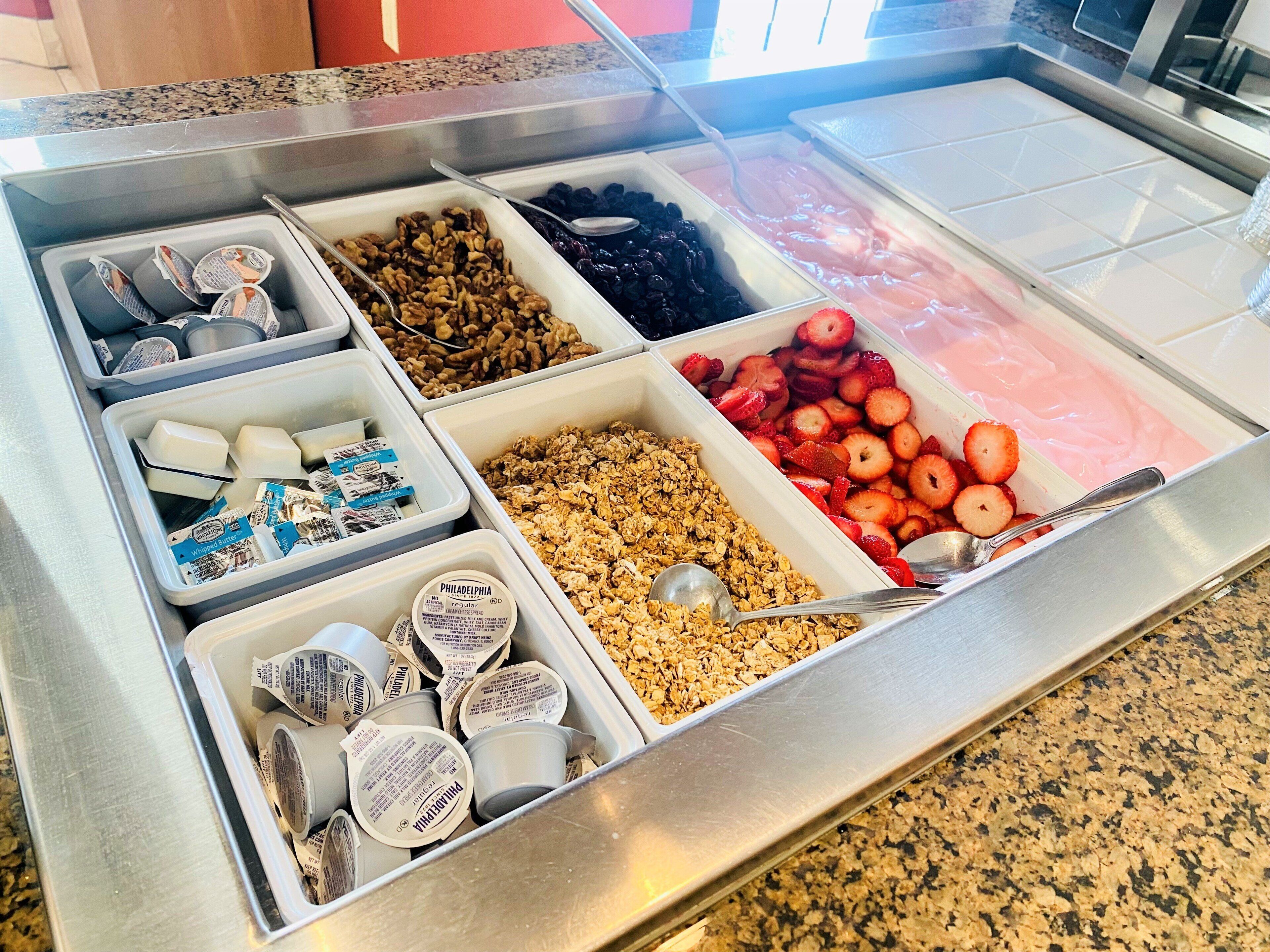 A breakfast buffet with various food options including yogurt, granola, fruits, and pastries.