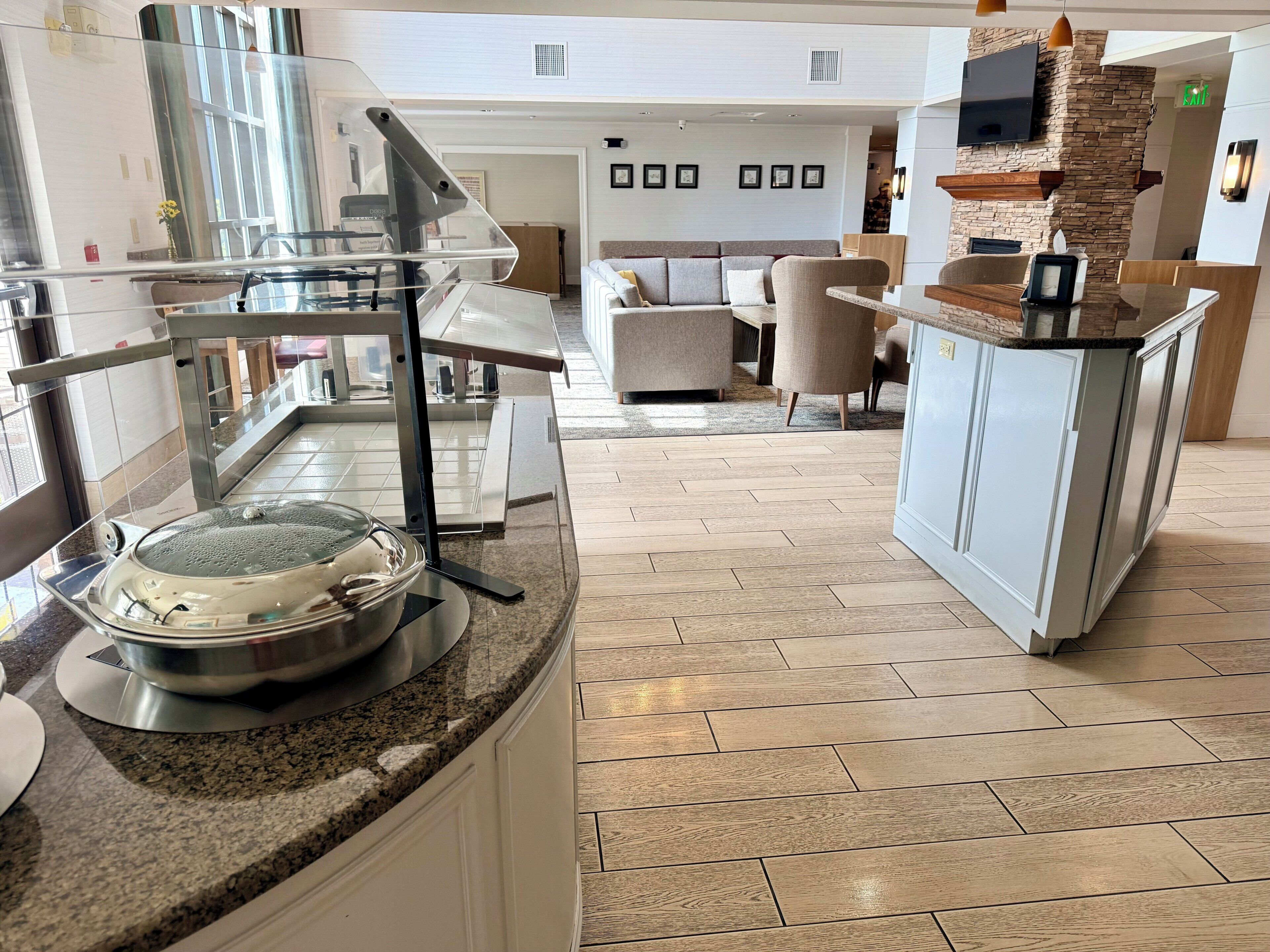 A modern kitchen with granite countertops, a stainless steel pot on the counter, and a dining area with a sofa and chairs.
