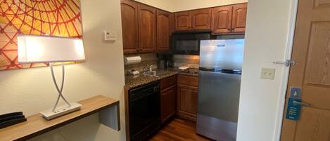A compact kitchen with wooden cabinets, a stainless steel refrigerator, and a microwave.