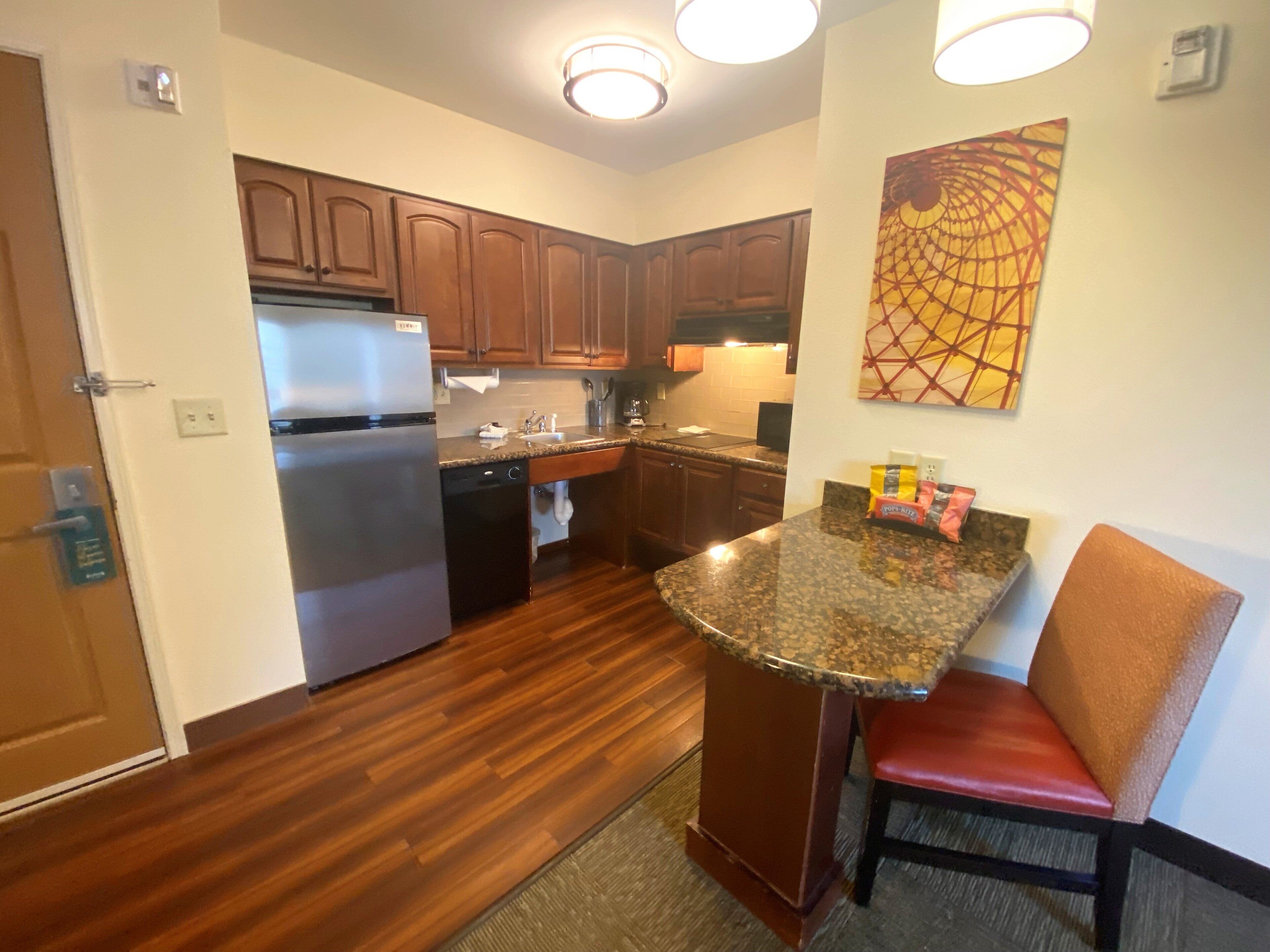A kitchen with wooden cabinets, a stainless steel refrigerator, a granite countertop, and a red chair.