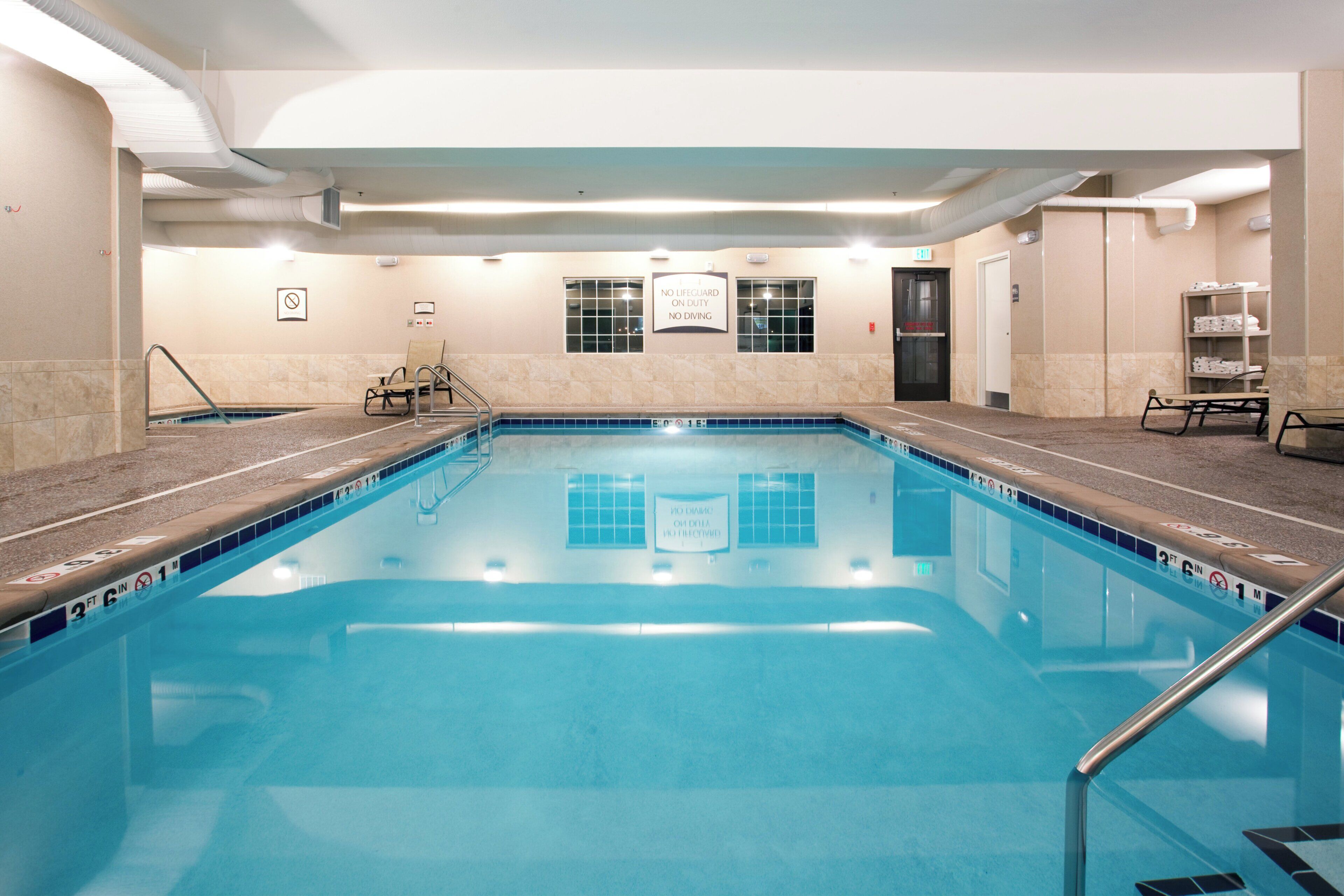 An indoor swimming pool with a tiled edge, a lifeguard sign, and a bench.