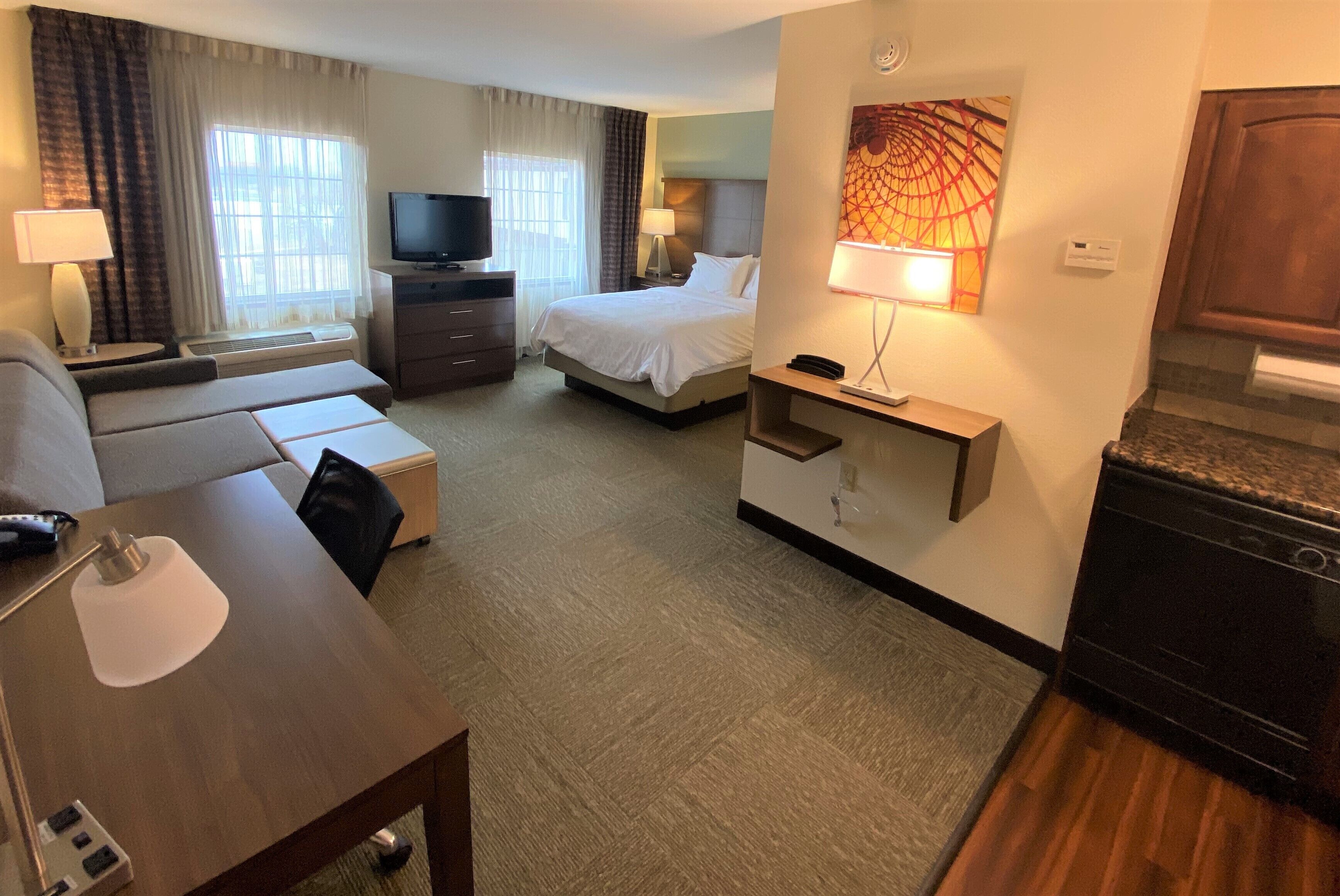 A hotel room with a bed, a sofa, a desk, a television, and a painting on the wall.