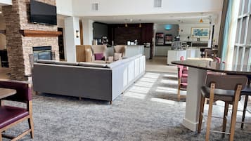A spacious living area with a stone fireplace, a large grey sofa, and a kitchen in the background.