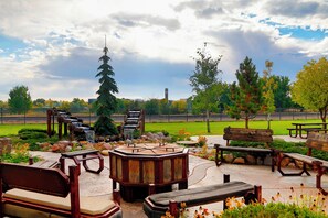 An outdoor seating area with wooden benches and a central fire pit. - Staybridge Suites Great Falls by IHG (Great Falls)