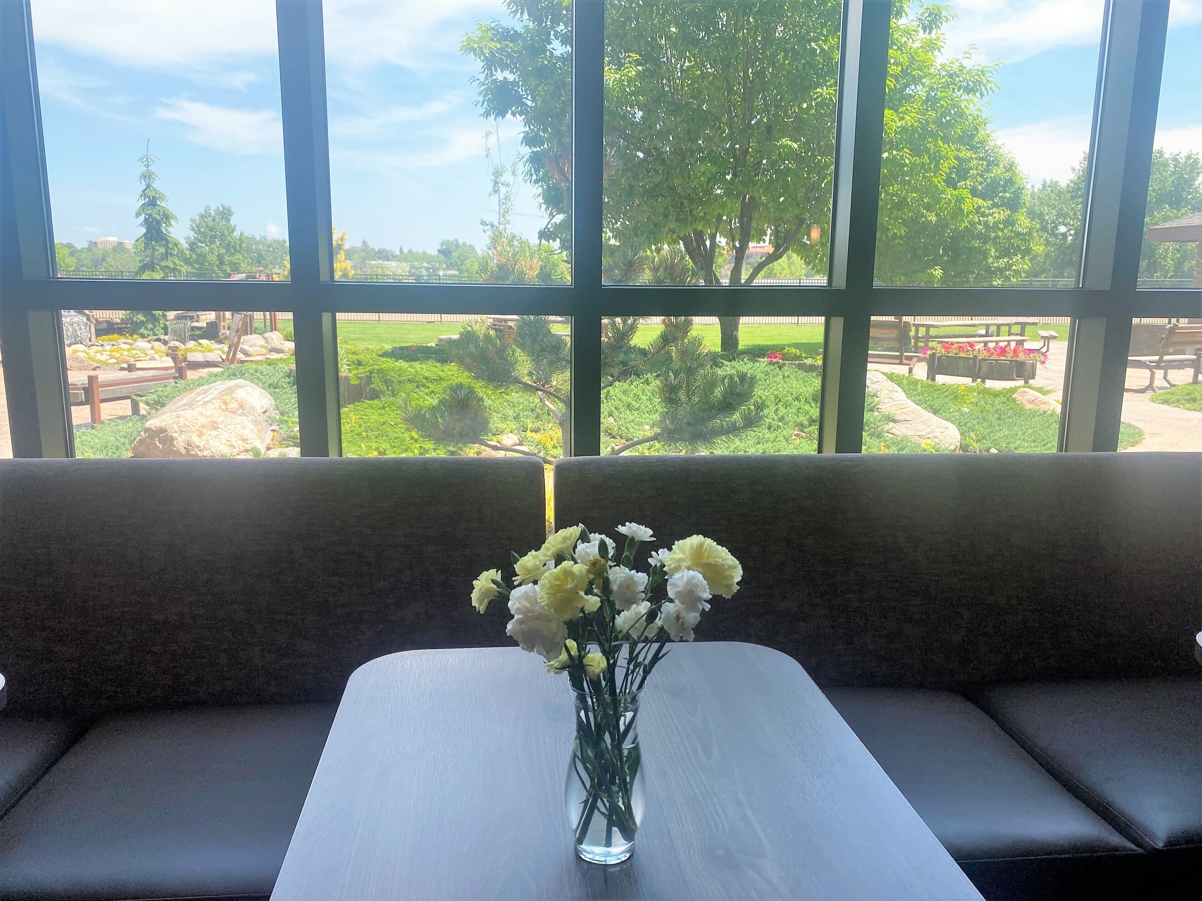 A room with a large window, a table with a vase of flowers, and a bench.