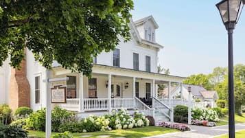 A white colonial-style building with a porch, a sign reading "The Charles Orvis Inn," and a well-maintained garden with various plants and flowers.
