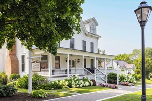 A white colonial-style building with a porch, a sign reading "The Charles Orvis Inn," and a well-maintained garden with various plants and flowers.