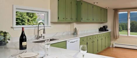 A modern kitchen with green cabinets, a marble countertop, and a view of the outdoors.