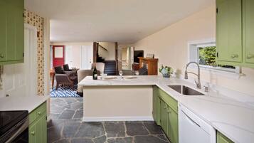 A kitchen with green cabinets, a marble countertop, and a stone floor.