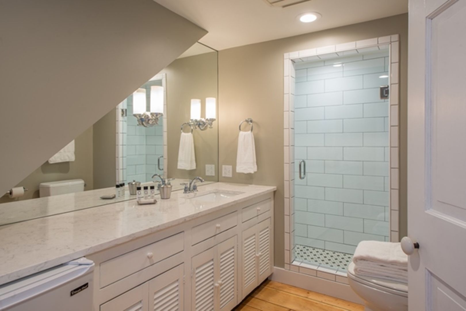 A modern bathroom with a large mirror, a walk-in shower, and a vanity with a sink and multiple drawers.
