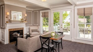 A room with a fireplace, a sofa, a dining table with chairs, and large windows offering a view of the outside.