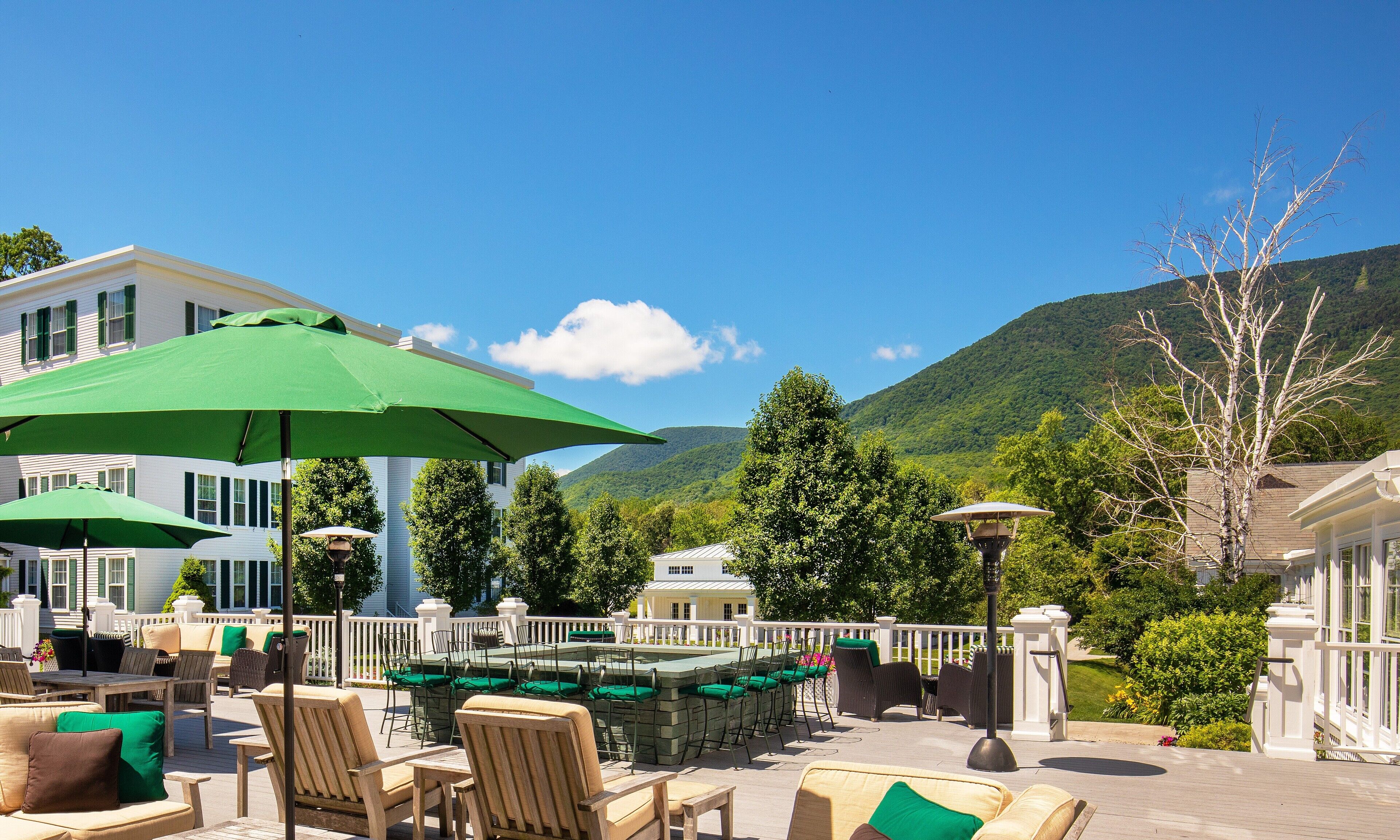 An outdoor patio area with tables and chairs, green umbrellas, and a view of a mountain.
