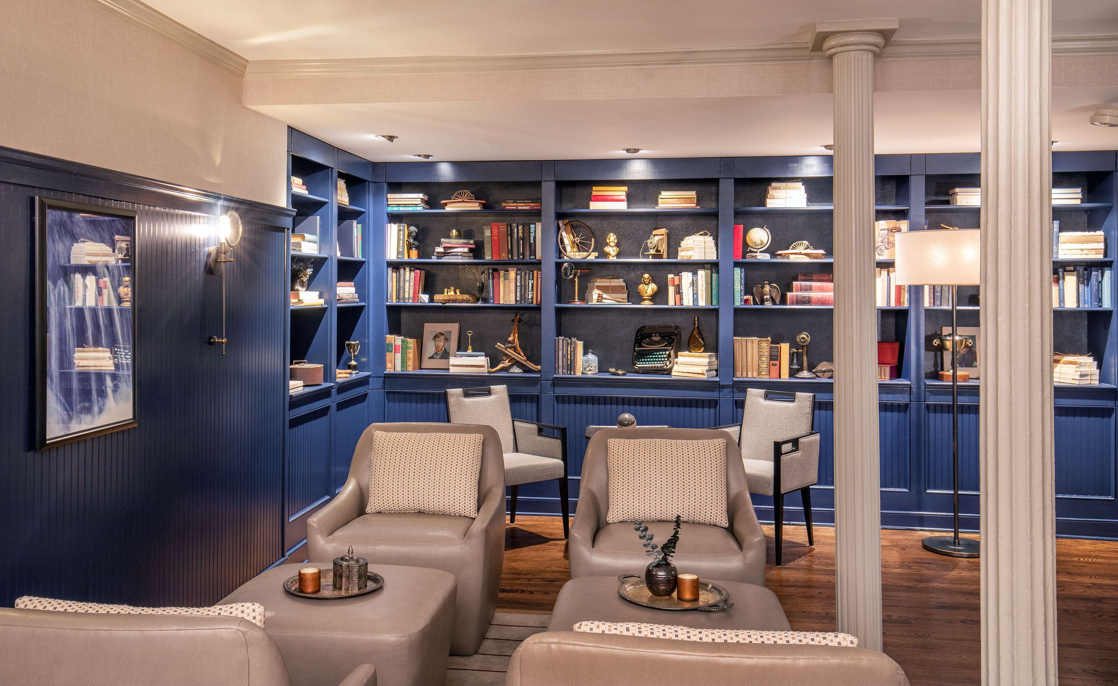 A library with dark blue bookshelves, leather chairs, and a wooden floor.
