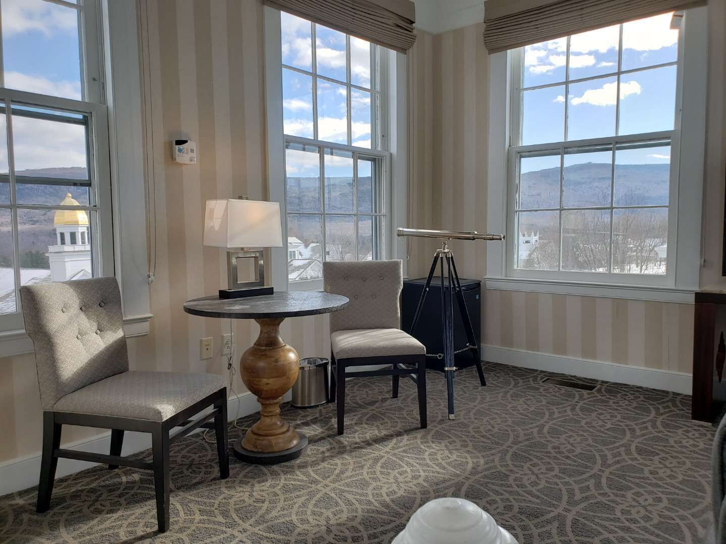 A room with large windows, a round table with a lamp, two chairs, and a telescope.