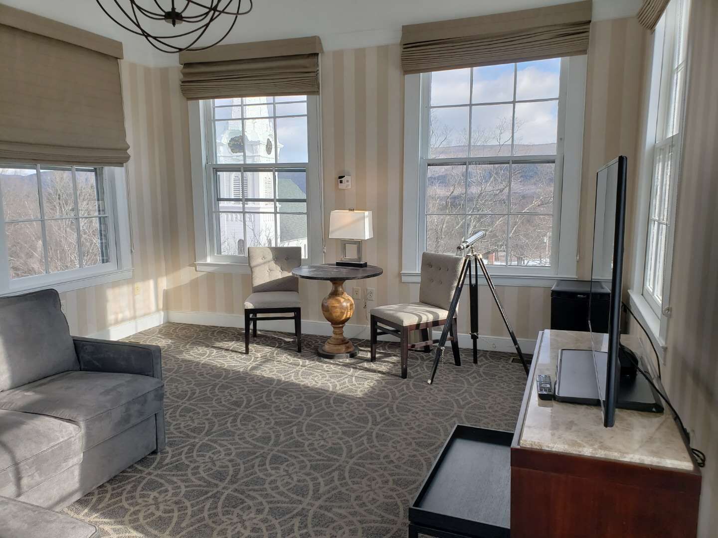 A well-lit room with a sofa, two chairs, a lamp, a telescope, and a TV on a stand.