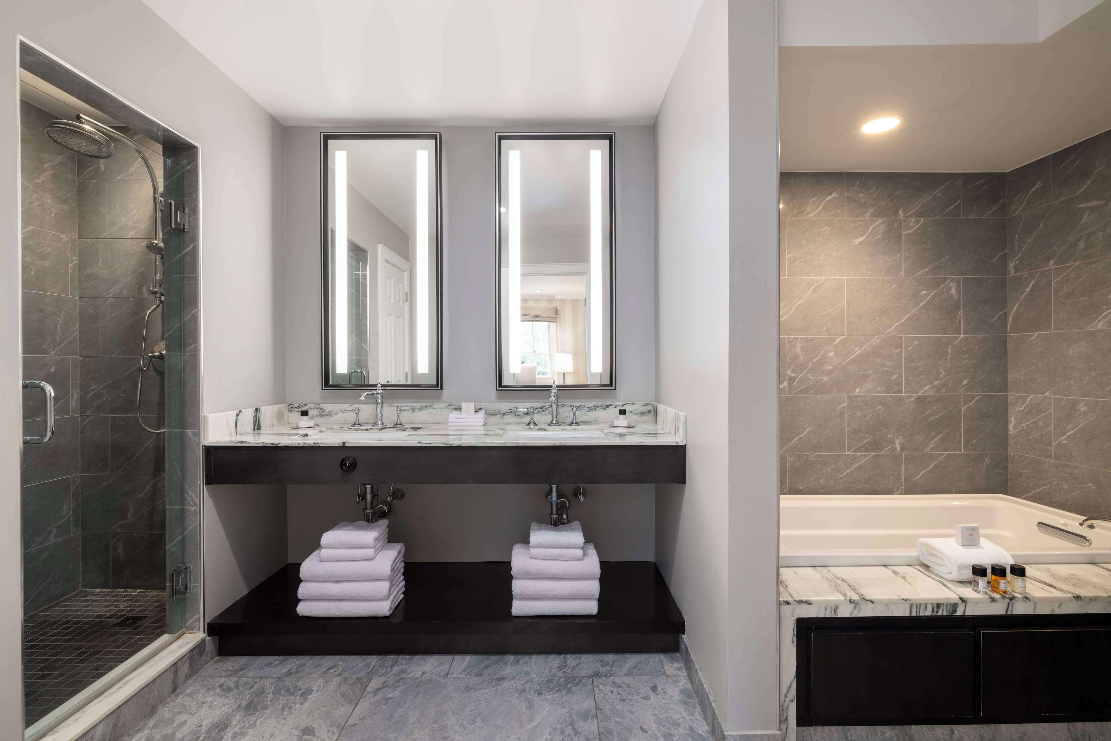 Un baño moderno con ducha envuelta en vidrio, lavamanos dobles, un espejo grande y una bañera independiente.