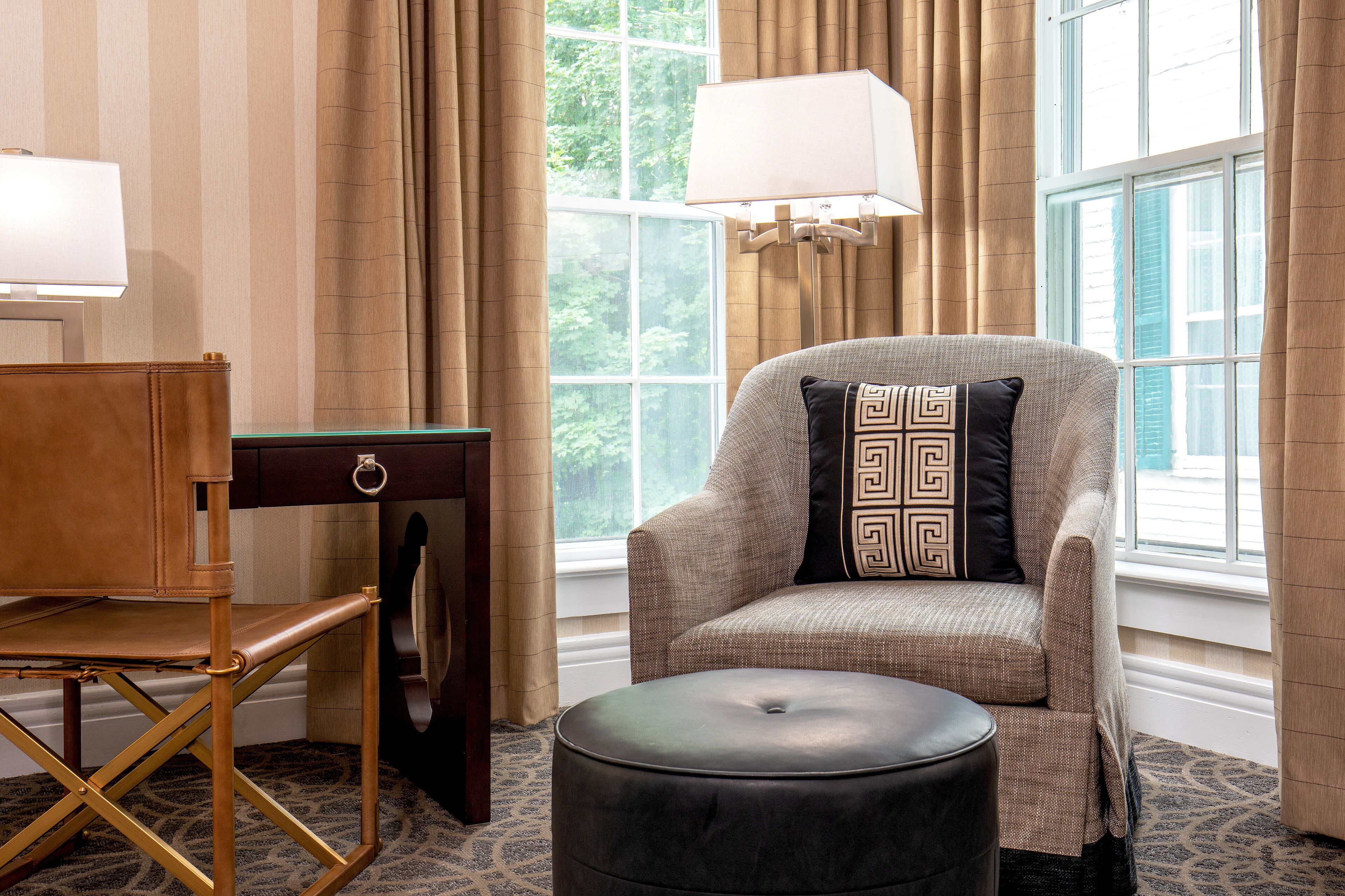 A cozy room with a cushioned armchair, a small wooden desk, and a round ottoman.