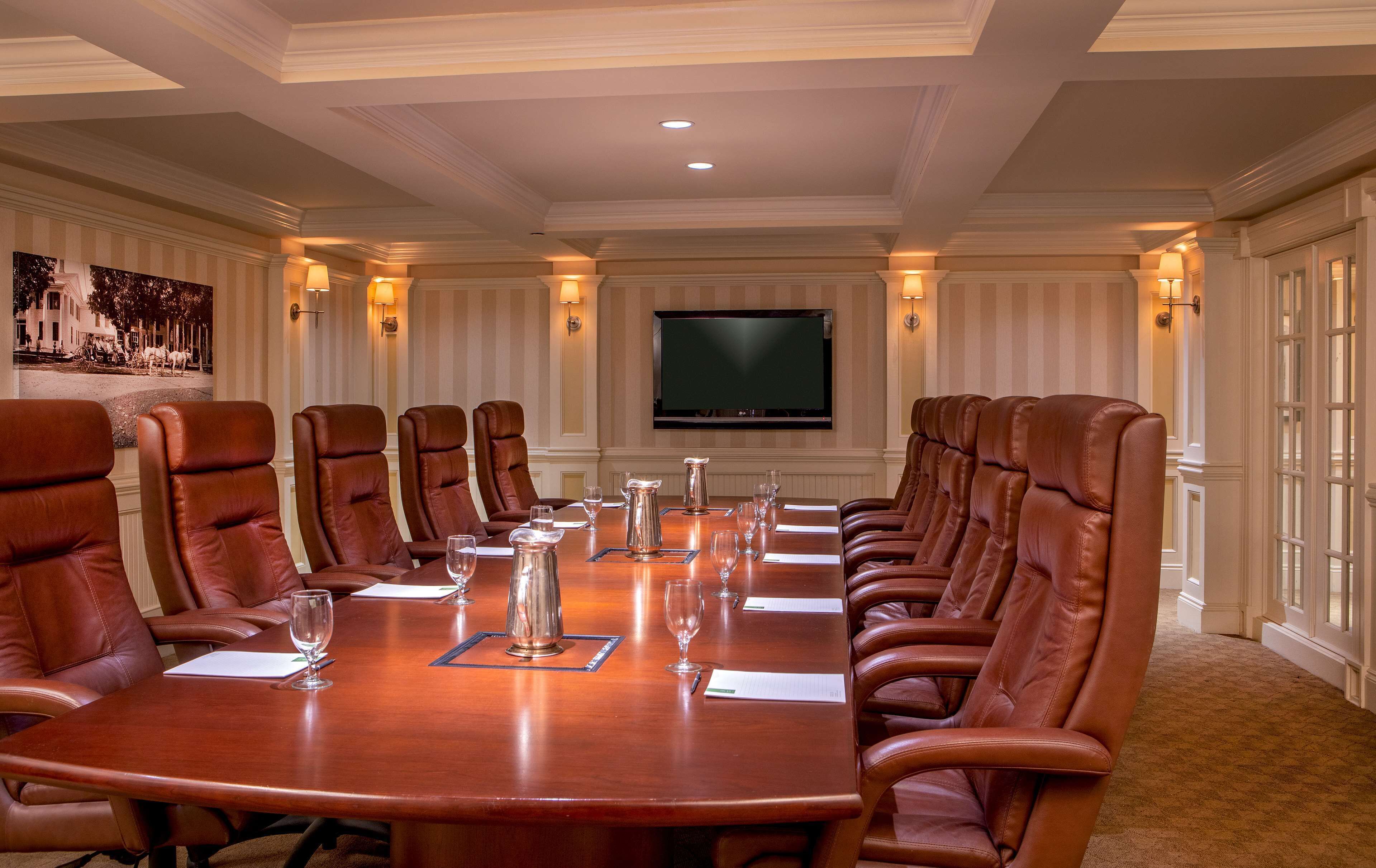 A conference room with a long table, leather chairs, a flat-screen TV, and wall-mounted lamps.
