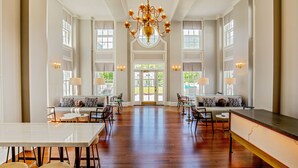 A spacious hotel lobby with a high ceiling, chandeliers, seating areas, and large windows.