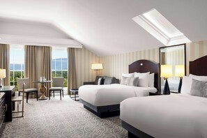 Quarto de hotel com duas camas, uma escrivaninha, cadeiras e varanda com vista.