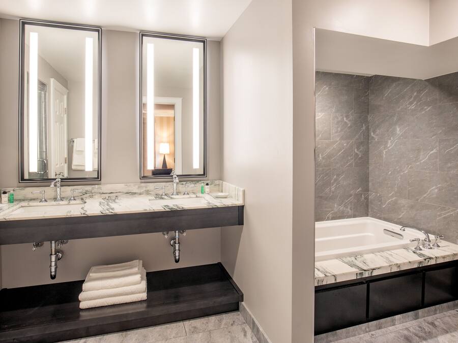 Ein modernes Badezimmer mit einem Waschtisch mit zwei Becken, einem großen Spiegel, einer Badewanne und Marmorböden.