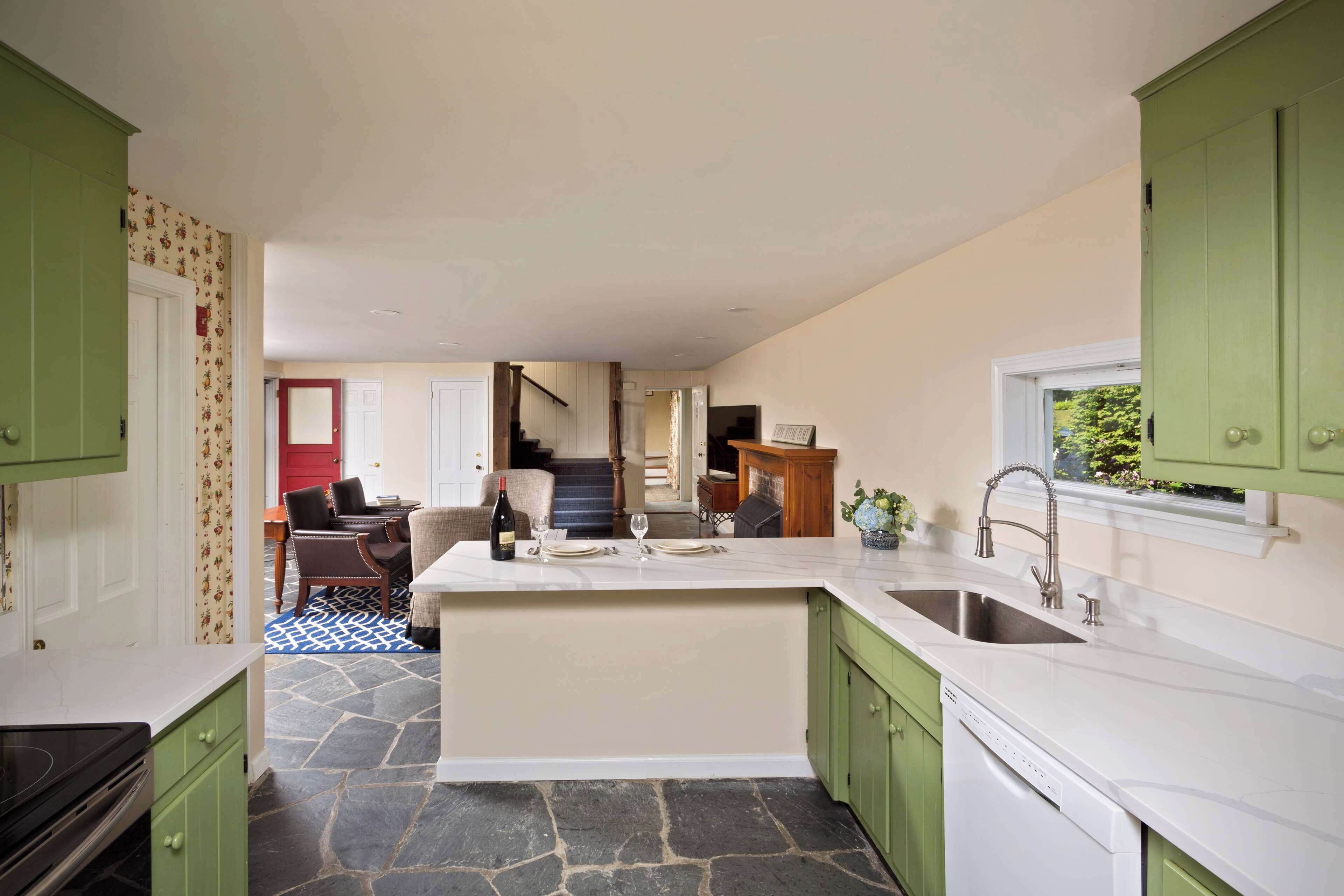 A kitchen with green cabinets, a marble countertop, and a stone floor.