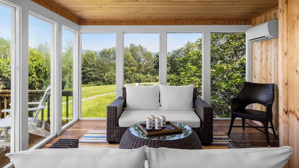 A covered patio area with a wicker sofa, a round table with drinks, and a chair.