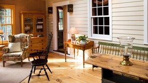 A cozy room with a wooden floor, a dining table with a lamp, a chair, a cabinet, and a window with curtains. - The Stockbridge Country Inn Closest B&B to Norman Rockwell Museum and Chesterwood (Stockbridge)