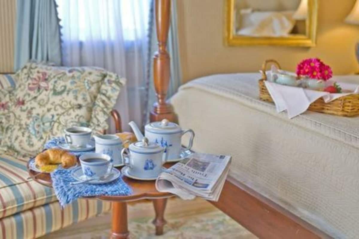 A breakfast setup with tea cups, a teapot, a croissant, and a newspaper on a tray.
