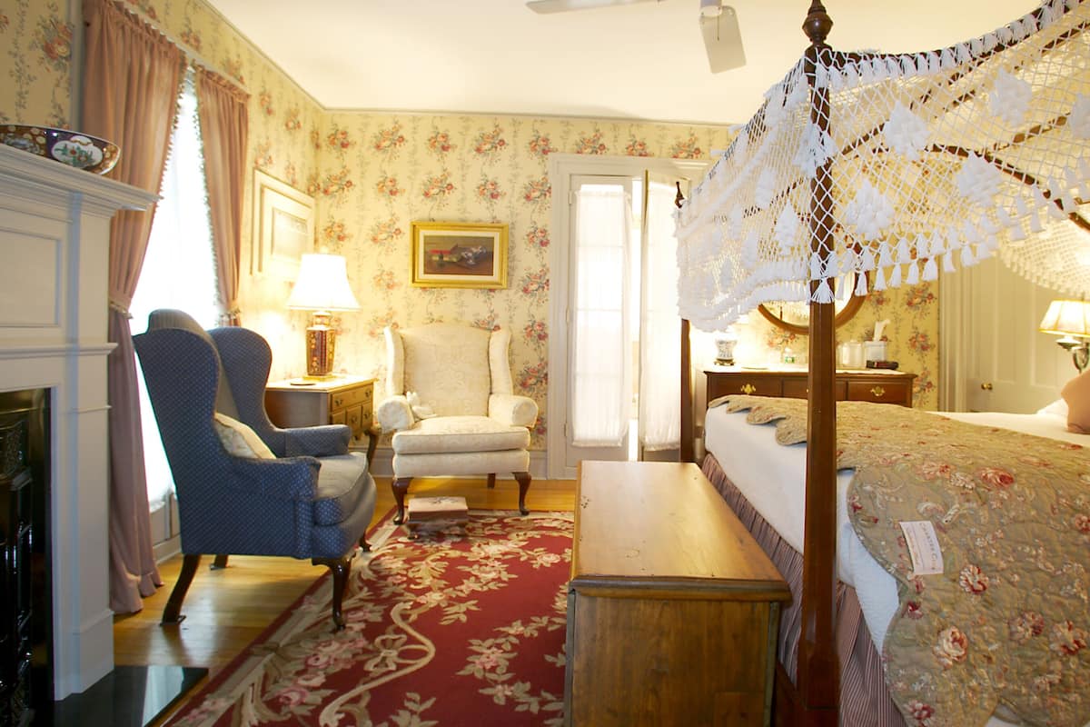A traditional bedroom with a four-poster bed, a fireplace, and floral wallpaper.