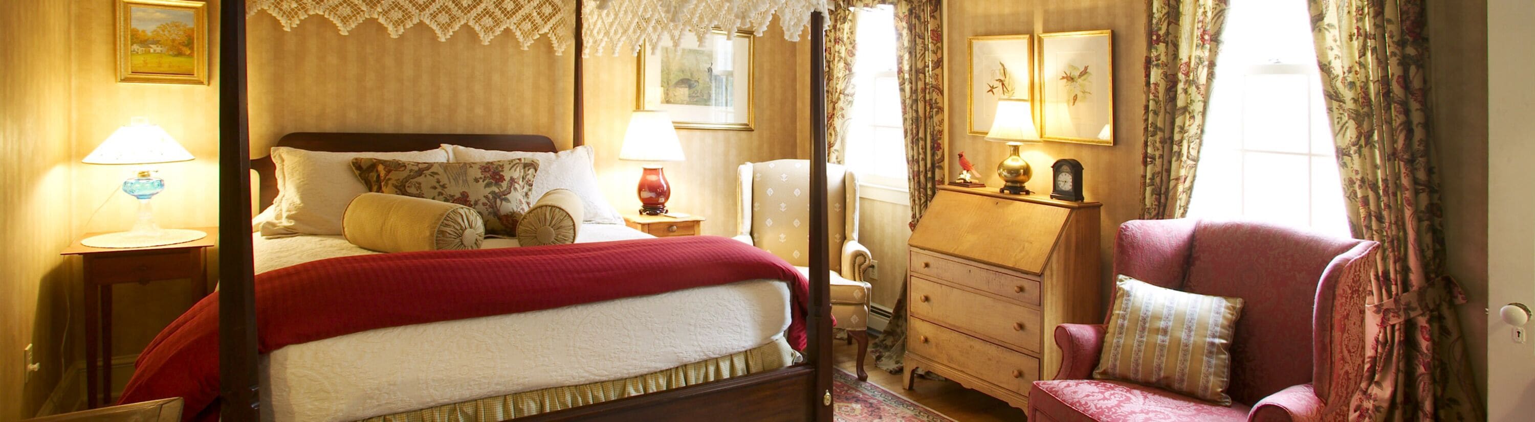 A traditional bedroom with a four-poster bed, a dresser, a chair, and a nightstand with lamps.