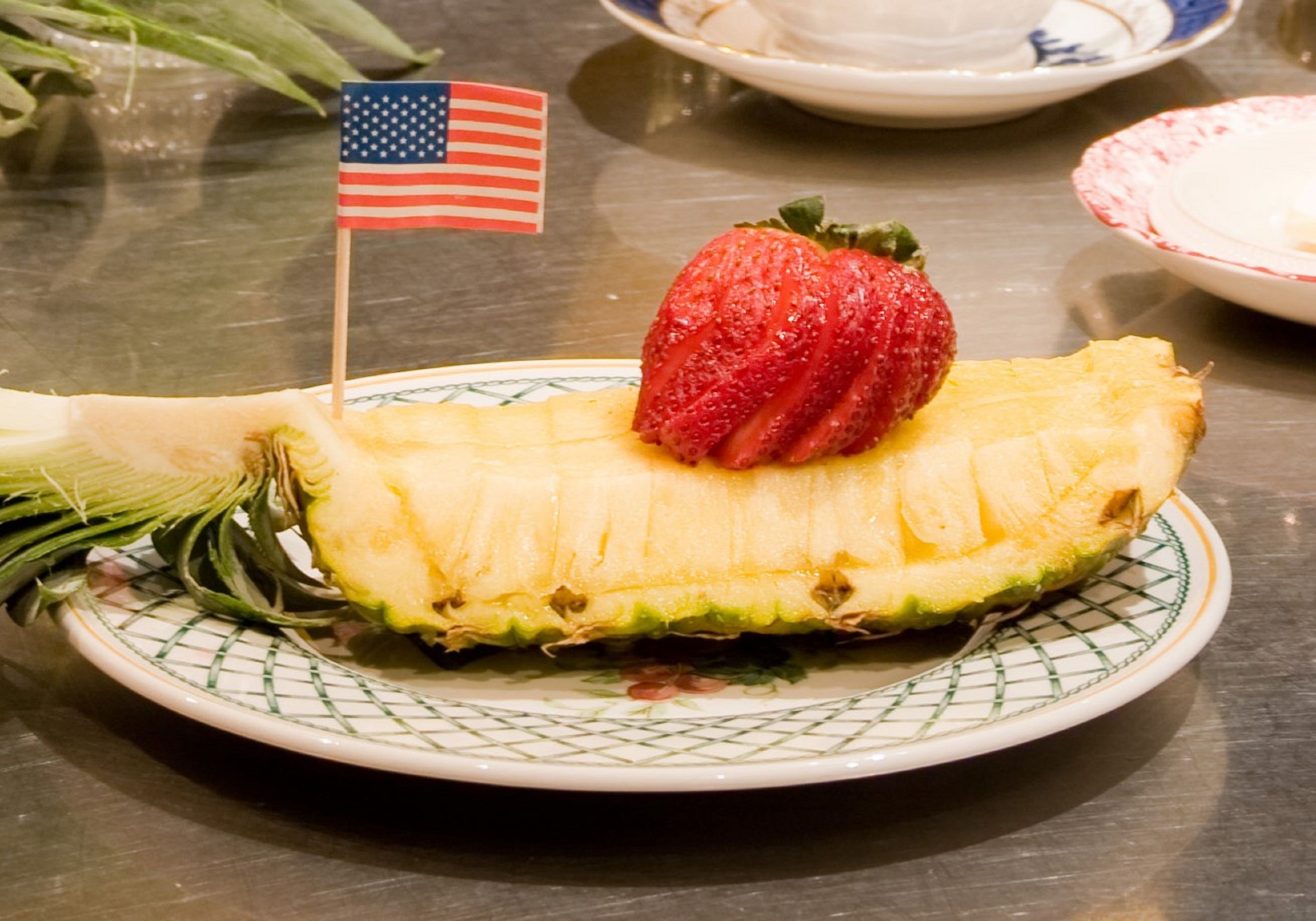 Un plato con media piña y una fresa encima, con una pequeña bandera estadounidense.