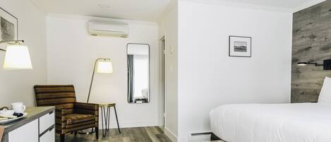 A hotel room with a bed, a desk, a chair, a mirror, and a wall-mounted picture.
