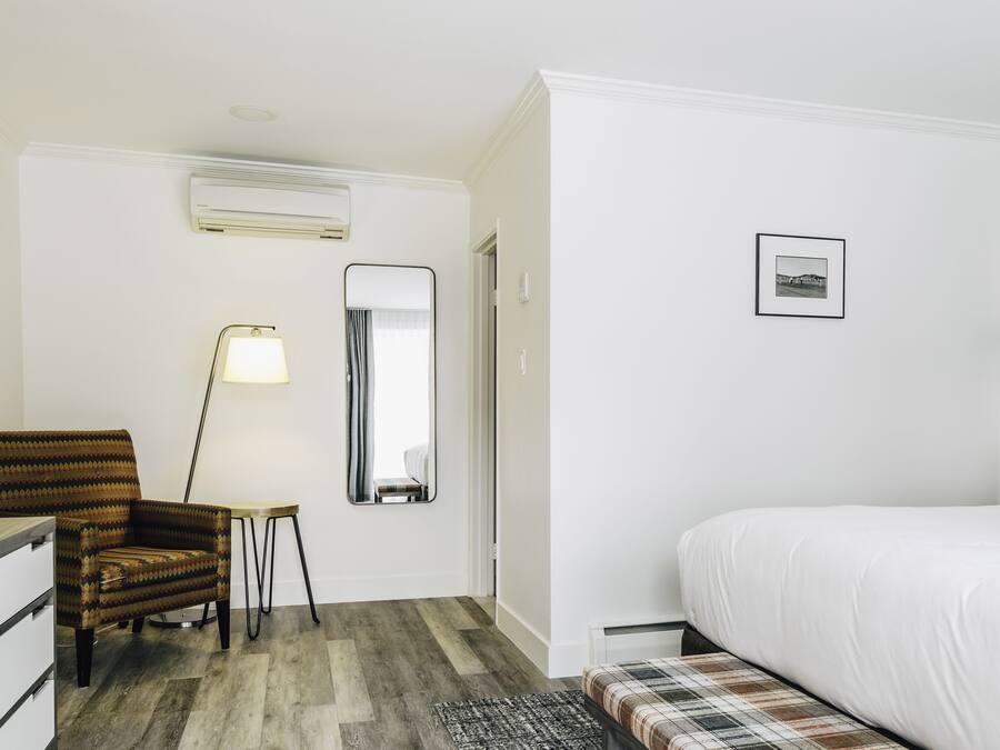 Habitación de hotel con cama, escritorio, silla, espejo y un cuadro colgado en la pared.