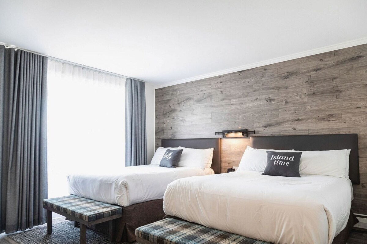 Habitación de hotel con dos camas, un banco, una pared decorativa de madera y una ventana con cortinas.