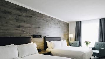 A hotel room with two beds, a nightstand with a lamp, a chair, and a window with curtains.