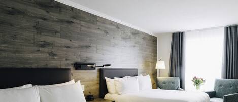 Ein Hotelzimmer mit zwei Betten, einem Nachttisch mit Lampe, einem Sessel und einem Fenster mit Vorhängen.
